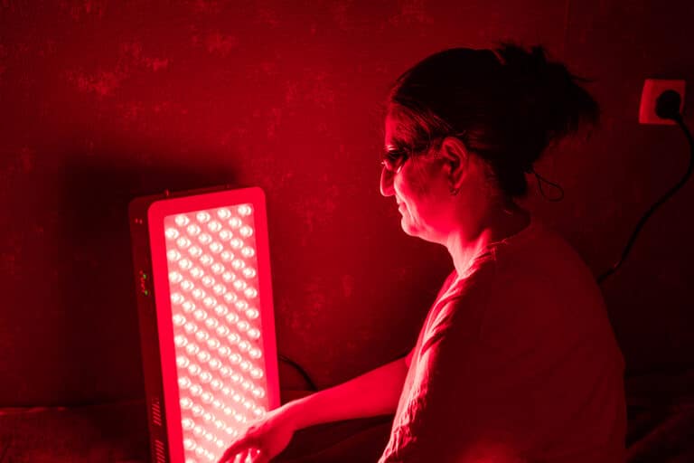 Senior Woman doing the Red Light Therapy Session with Panel and wearing eye protection at home on the bed